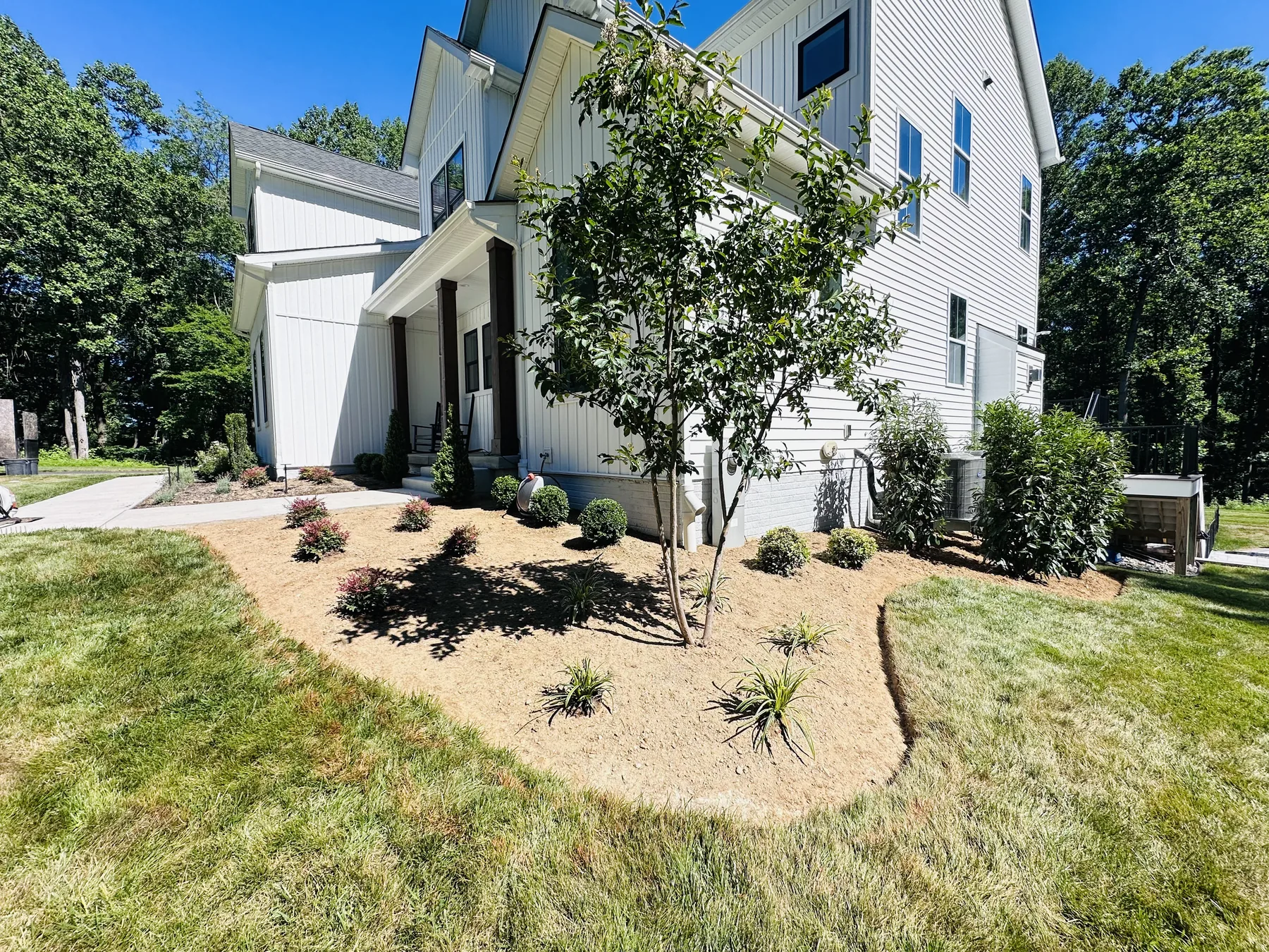 Freshly installed planting bed with a young tree and shrubs beside a Harford County home